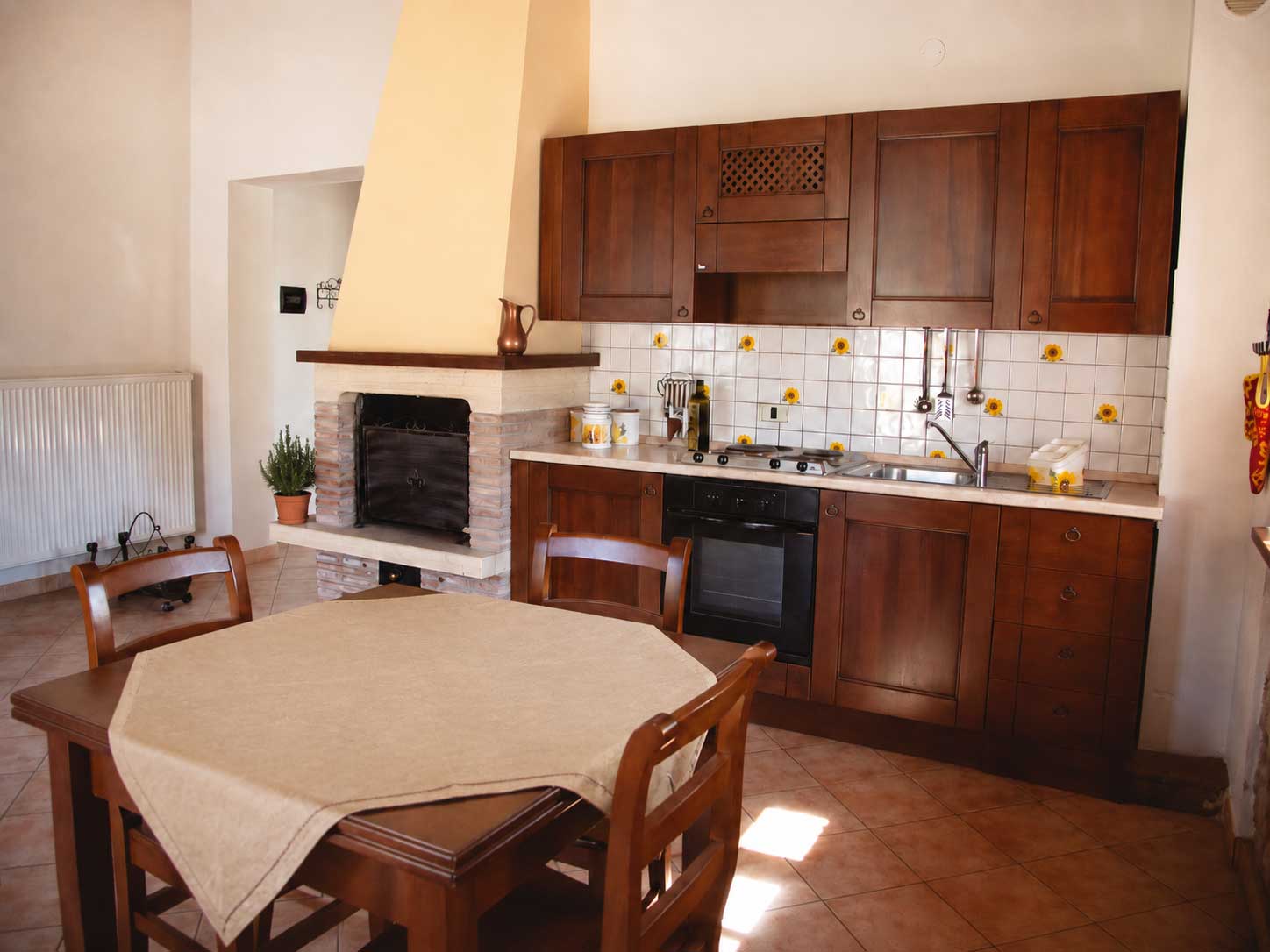 The cozy rustic kitchen of the Girasole apartment in the Umbrian farmhouse Domus Santa Croce, with a fireplace, wooden furniture, and a warm atmosphere, is ideal for Italian tourists.