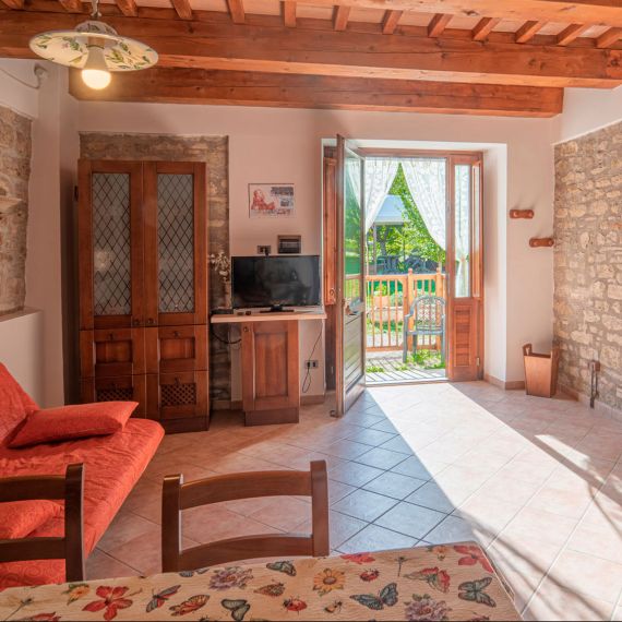 Luminoso soggiorno agriturismo in Umbria, travi a vista, accesso a giardino, ideale per rilassarsi nell'atmosfera rustica.