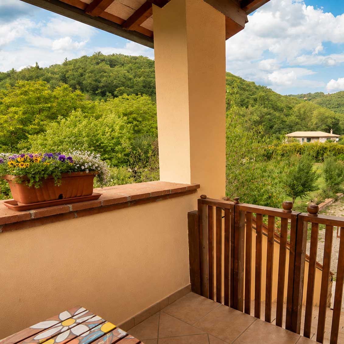 Vista panoramica da un balcone fiorito dell'agriturismo umbro, immerso nel verde delle colline circostanti.